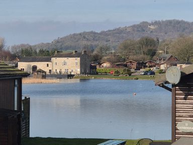 A lake with buildings and cars near the shore and hills in the background at Sunset Retreat South Lakeland Leisure Village near Carnforth