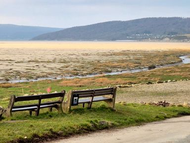 Two wooden benches on grass overlooking a large tidal flat with hills in the background at Sunset Retreat in South Lakeland Leisure Village near Carnforth