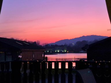 A lake with houses and hills in the background at sunset at Sunset Retreat South Lakeland Leisure Village near Carnforth