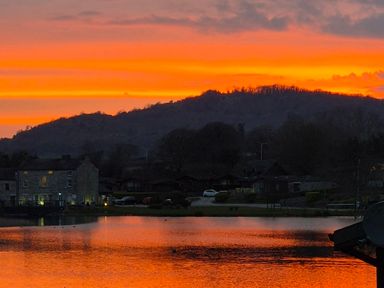 A lake reflecting an orange sunset with houses and hills in the background at Sunset Retreat South Lakeland Leisure Village near Carnforth