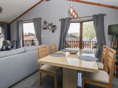 A dining area with a wooden table and chairs next to a sitting area with sofas and large windows at Sunset Retreat South Lakeland Leisure Village near Carnforth