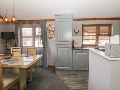 A dining area with wooden table and chairs next to a kitchen with gray cabinets at Sunset Retreat in South Lakeland Leisure Village near Carnforth