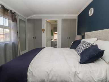 A bedroom with a bed and pillows two closets a door leading to a bathroom and a window with curtains at Sunset Retreat in South Lakeland Leisure Village near Carnforth