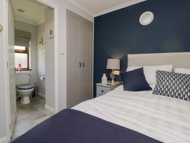 A bedroom with a bed and bedside table with lamp and an ensuite bathroom at Sunset Retreat South Lakeland Leisure Village near Carnforth