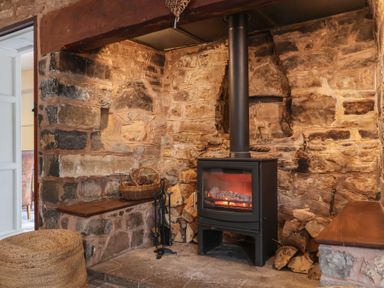 A wood burning stove with firewood and tools in a stone fireplace at Dragon House in Bilbrook near Minehead