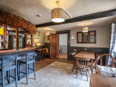 A room with a bar counter and blue bar stools wooden tables and chairs stained glass windows at Dragon House in Bilbrook near Minehead
