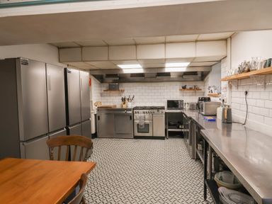 A kitchen with stainless steel appliances and counters and wooden table and chairs at Dragon House in Bilbrook near Minehead