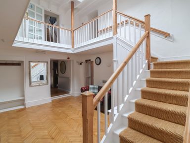 A staircase with carpeted steps and wooden banister in a hallway with wooden floor and white walls at Dragon House in Bilbrook near Minehead