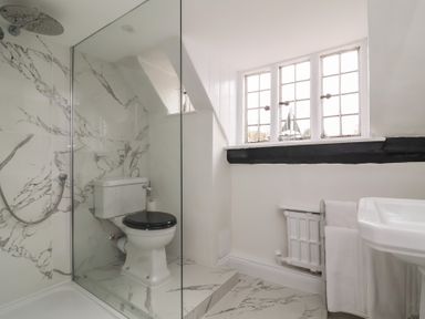 A bathroom with a shower, toilet, sink, window, and radiator with towels at Dragon House in Bilbrook near Minehead