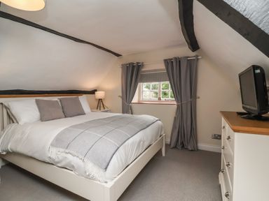 A bedroom with a double bed bedside table with lamp curtained window and a dresser with a TV at Dragon House in Bilbrook near Minehead