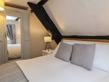 A bedroom with a bed with gray pillows a bedside table with a lamp and a wardrobe with a mirrored door at Dragon House in Bilbrook near Minehead