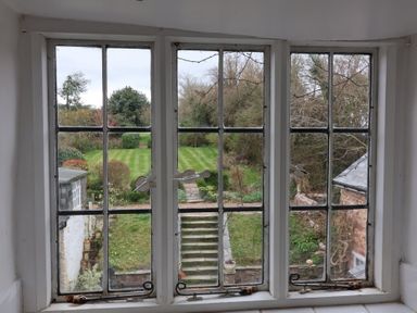 A garden with grass stairs and shrubs viewed through a window at Dragon House in Bilbrook near Minehead