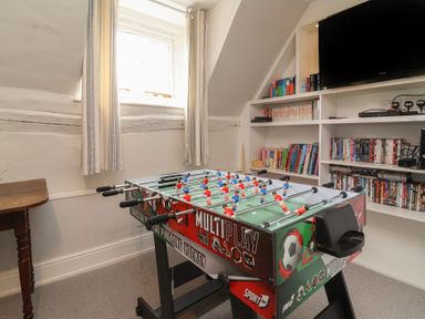 A game room with a foosball table under a window and shelves filled with books dvds and a television at Dragon House in Bilbrook near Minehead