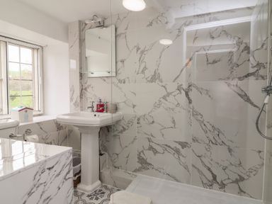 A bathroom with a pedestal sink mirror toilet window and a shower area with marble tiles at Dragon House in Bilbrook near Minehead
