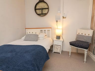 A bedroom with a single bed side table with lamp and a chair with cushions at Dragon House in Bilbrook near Minehead