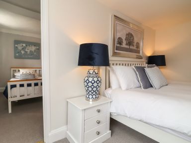A bedroom with a white bed and pillows two bedside tables with lamps and a framed picture of trees on the wall at Dragon House in Bilbrook near Minehead