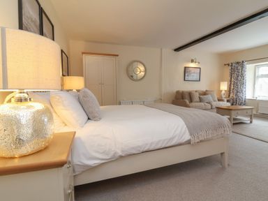 A bedroom with a bed a sofa a wardrobe and a window with curtains at Dragon House in Bilbrook near Minehead