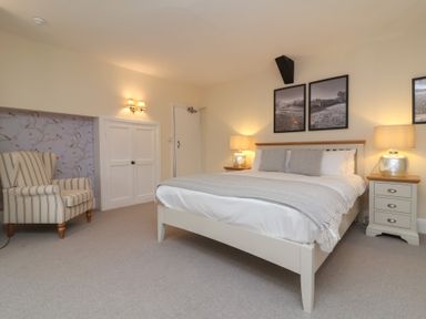 A bedroom with a bed and two bedside tables with lamps and a striped armchair at Dragon House in Bilbrook near Minehead
