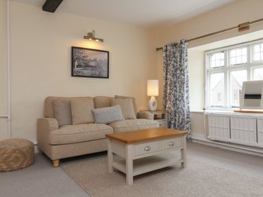 A living room with a beige sofa coffee table lamp and window at Dragon House in Bilbrook near Minehead