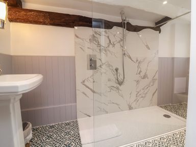 A bathroom with a walk-in shower featuring marble wall tiles a pedestal sink patterned floor tiles and exposed wooden beams at Dragon House in Bilbrook near Minehead