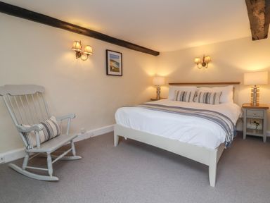 A bedroom with a bed bedside tables lamps wall sconces and a rocking chair at Dragon House in Bilbrook near Minehead