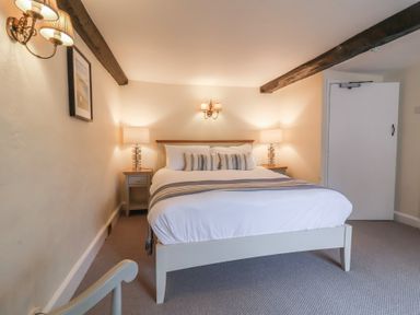 A bedroom with a double bed two bedside tables with lamps exposed wooden ceiling beams and a wall lamp at Dragon House in Bilbrook near Minehead