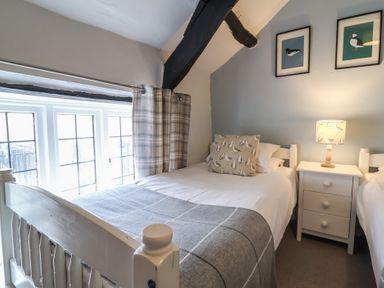 A bedroom with two single beds a nightstand with a lamp and bird pictures on the wall at Dragon House in Bilbrook near Minehead