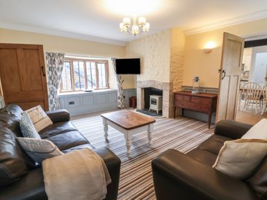 A living room with two leather sofas a wooden coffee table a fireplace and a wall mounted television at Dragon House in Bilbrook near Minehead