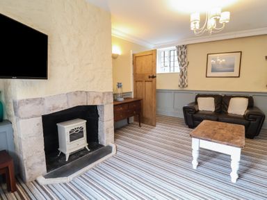 A living room with a stone fireplace a leather sofa a wooden coffee table and a television at Dragon House in Bilbrook near Minehead
