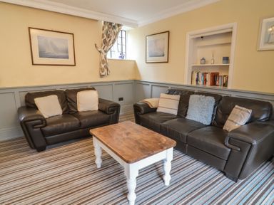 A sitting room with two brown leather sofas a wooden coffee table striped carpet and framed pictures at Dragon House in Bilbrook near Minehead