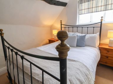 A bedroom with a metal bed frame two bedside tables with lamps and a window with striped blinds at Dragon House in Bilbrook near Minehead