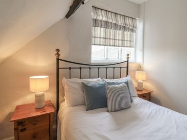 A bedroom with a bed with white bedding and pillows two bedside tables with lamps and a window with a striped blind at Dragon House in Bilbrook near Minehead