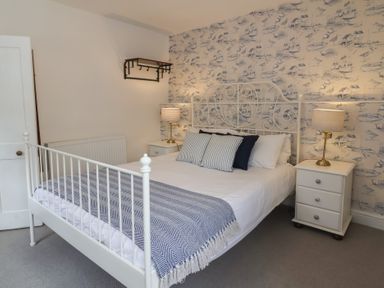 A bedroom with a white metal bed frame two bedside tables with lamps and patterned wallpaper at Dragon House in Bilbrook near Minehead