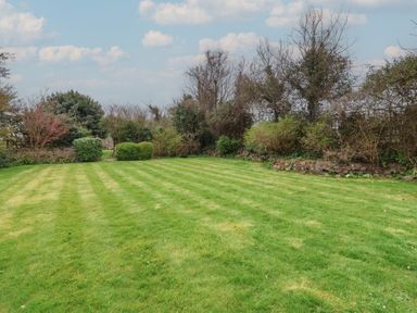 A large grassy lawn bordered by various bushes and trees under a partly cloudy sky