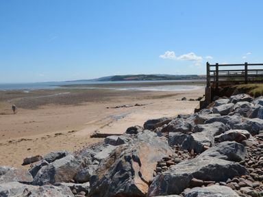 A sandy beach with large rocks and a wooden fence near the shore at Dragon House in Bilbrook near Minehead