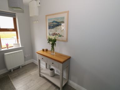 A hallway with a console table holding flowers and decorations and a window with a garden view at C65 Cahermore Holiday Village in Enniscrone County Sligo