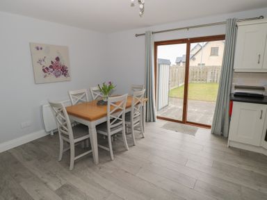 A dining area with a wooden table and six chairs next to sliding glass doors leading to a garden at C65 Cahermore Holiday Village in Enniscrone County Sligo