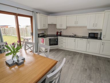 A kitchen with white cabinets black countertop a wooden dining table with chairs and purple flowers in a vase at C65 Cahermore Holiday Village Enniscrone County Sligo