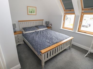 A bedroom with a double bed between two bedside tables with lamps and two windows at C65 Cahermore Holiday Village in Enniscrone County Sligo