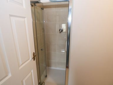 A shower cubicle with glass doors and beige tiled walls at C65 Cahermore Holiday Village in Enniscrone County Sligo