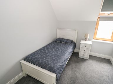 A single bed with geometric patterned bedding next to a three drawer bedside table with a lamp under a window in a bedroom at C65 Cahermore Holiday Village in Enniscrone County Sligo