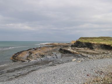 Rocky coastline with cliffs and pebble beach under cloudy sky at C65 Cahermore Holiday Village in Enniscrone County Sligo