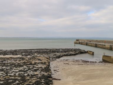 A rocky and sandy seashore with a concrete pier and calm water at C65 Cahermore Holiday Village in Enniscrone County Sligo