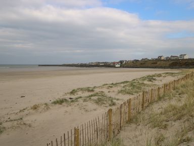 A sandy beach with grassy dunes and a wooden fence near a small town by the sea at C65 Cahermore Holiday Village in Enniscrone County Sligo