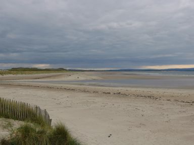 A sandy beach with dunes and a wooden fence under a cloudy sky at C65 Cahermore Holiday Village in Enniscrone County Sligo