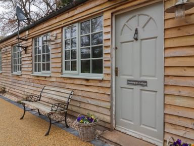 An exterior view of a wooden cottage with three windows a bench and a door labeled Gatekeepers Cottage at Bilbrook near Minehead