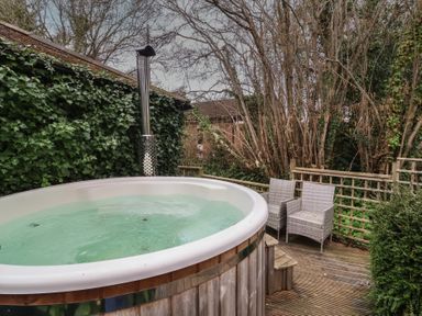 An outdoor hot tub on a wooden deck with two wicker chairs surrounded by trees and ivy at Gatekeeper's Cottage in Bilbrook near Minehead
