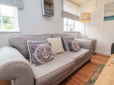 A gray fabric sofa with decorative pillows near two windows and a floor lamp in a living room at Gatekeeper's Cottage Bilbrook near Minehead