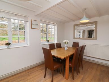 A dining room with a wooden table and six brown chairs at Gatekeeper's Cottage Bilbrook near Minehead
