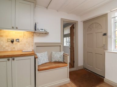 An entryway with a wooden door a bench with cushions and kitchen cabinets at Gatekeeper's Cottage in Bilbrook near Minehead